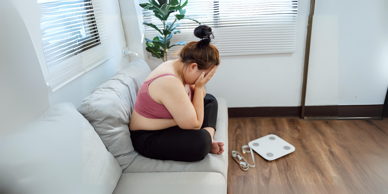 overweight woman on couch, weight scale on floor nearby