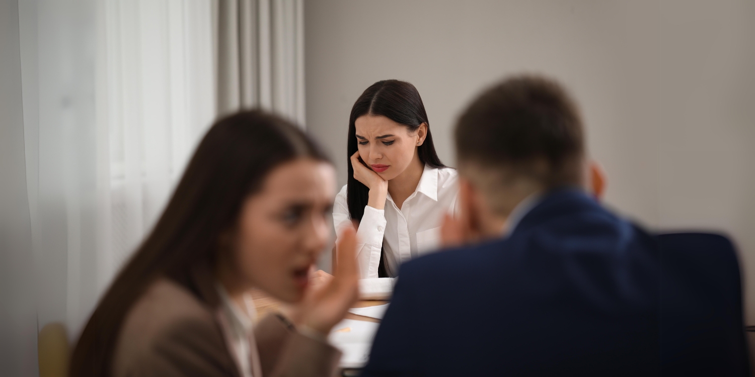 two coworkers whispering with a sad woman in the background