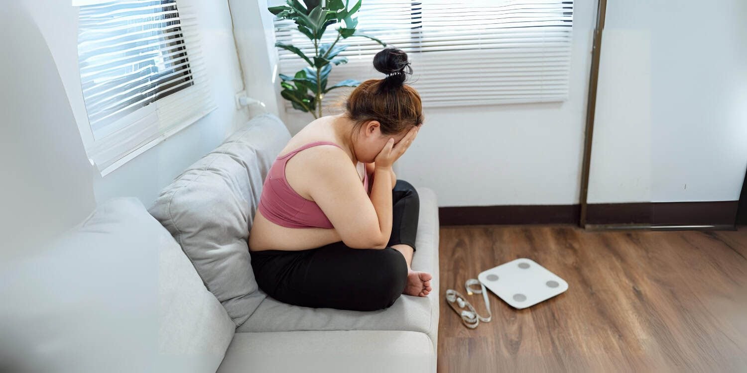overweight woman on couch, weight scale on floor nearby